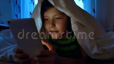 晚上，小男孩在<strong>被子</strong>下，拿着一台数字平板电脑玩网络游戏。 7岁<strong>儿童</strong>使用智能手机